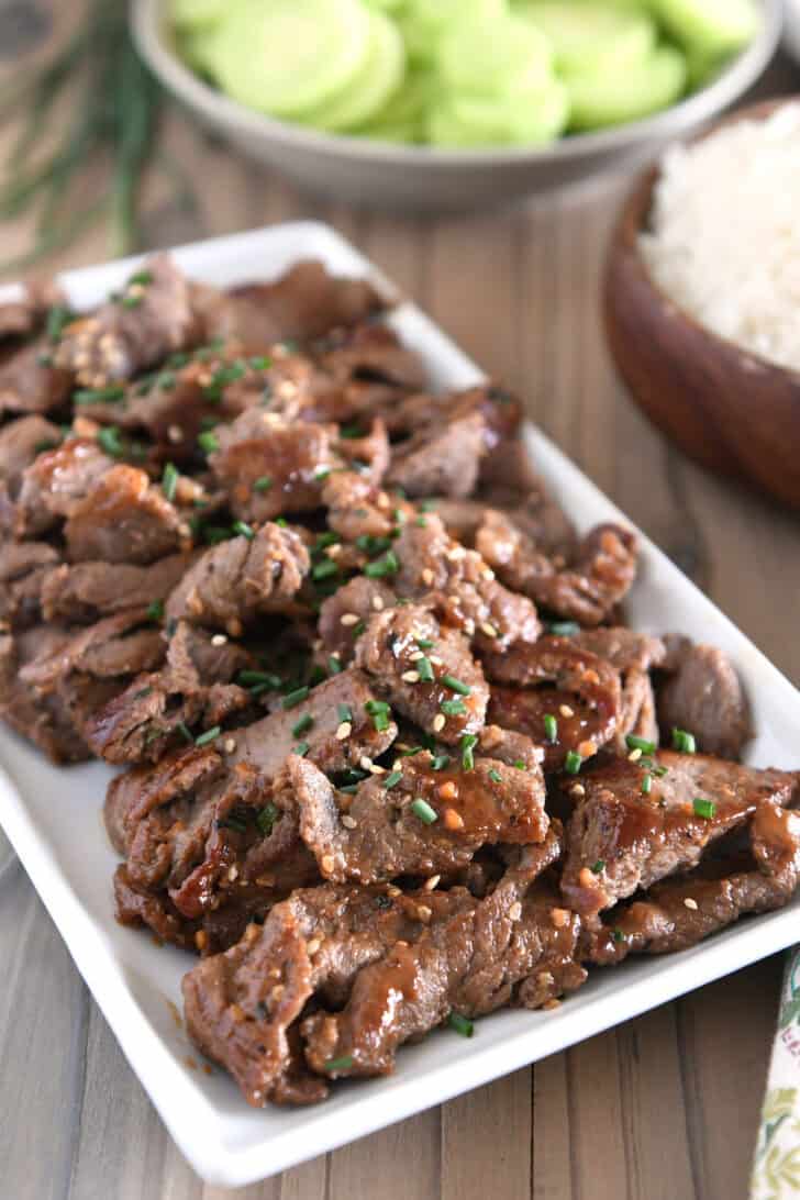 White tray with pieces of cooked beef, Korean sauce, green onions and sesame seeds.