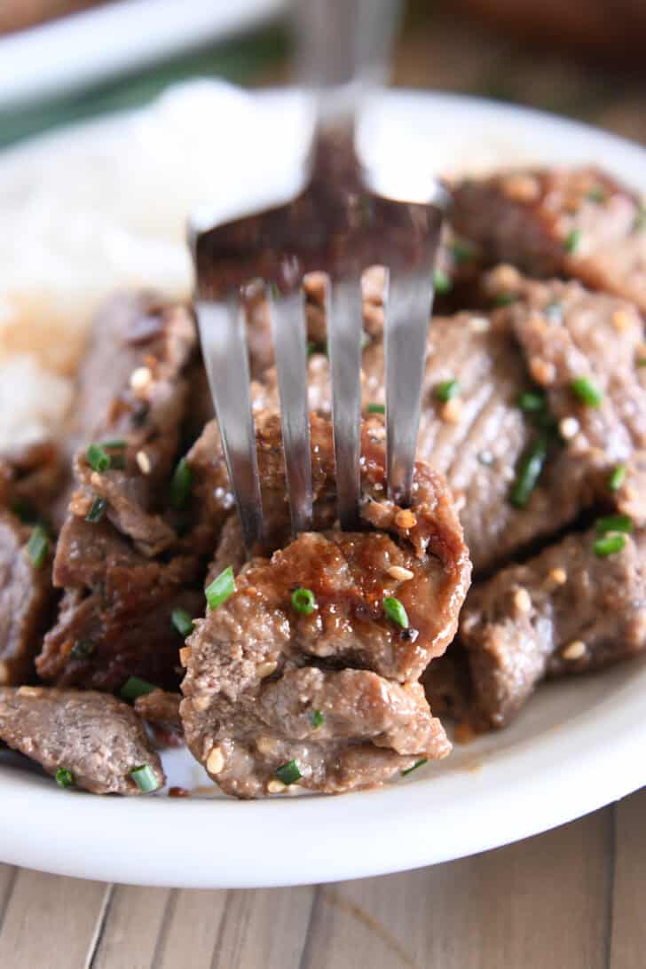 Fork piercing piece of cooked beef bulgogi.