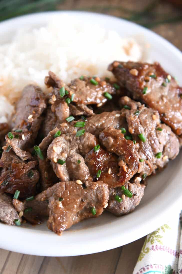 White plate with white rice and several pieces of Korean beef bulgogi, green onions and sesame seeds.