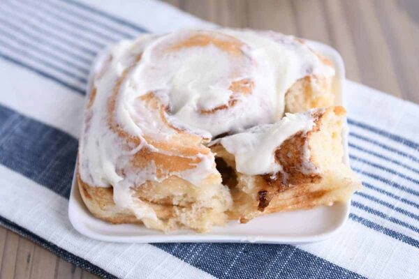 A frosted cinnamon roll on a square white plate.